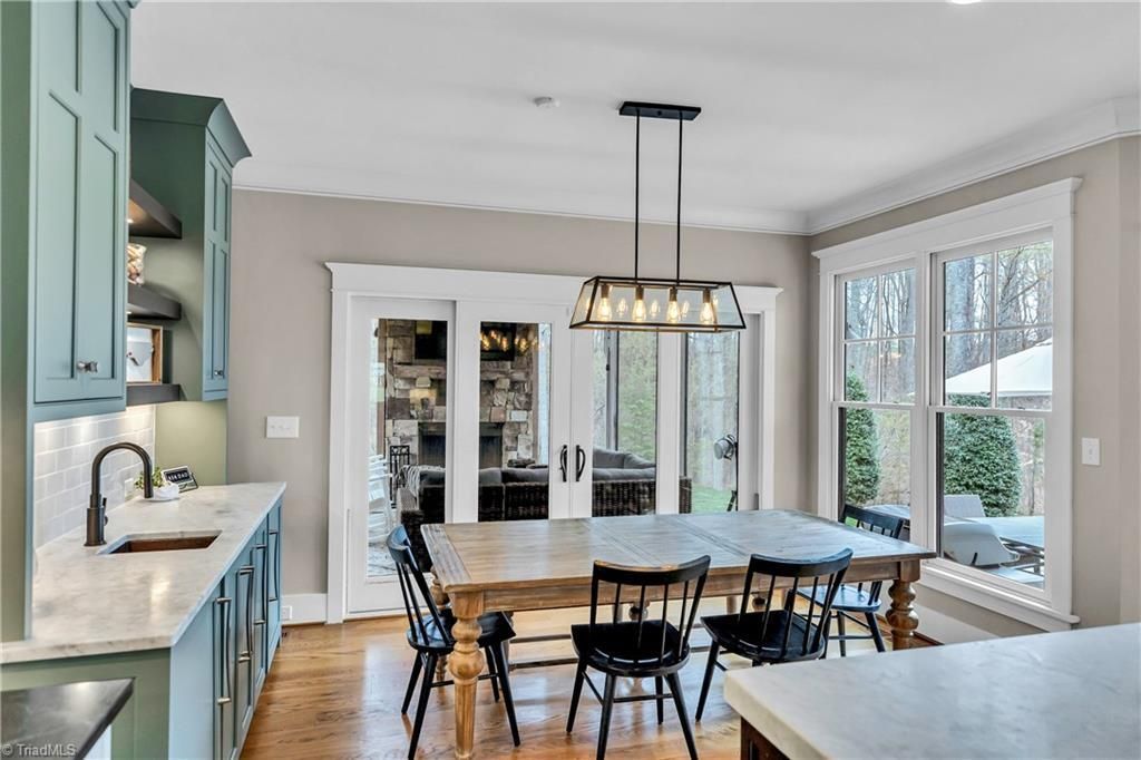 Bright kitchen with light wood island, black chairs, teal cabinets, and large windows by a dining table