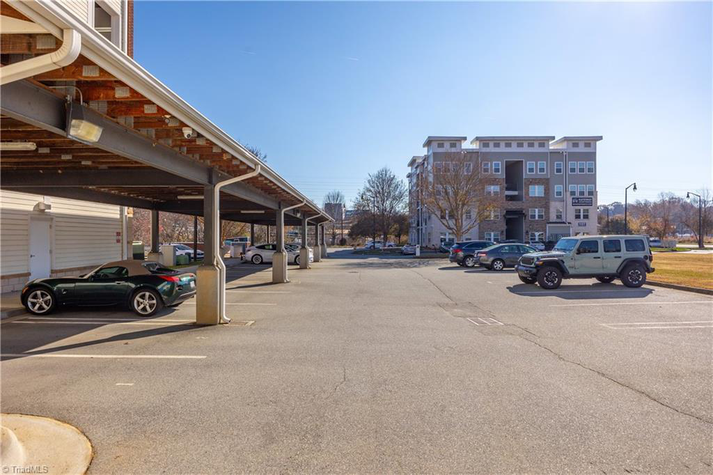 A parking lot with cars parked under a canopy and a building in the background.