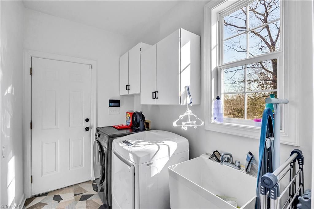 Bright laundry room with white cabinets, washer and dryer, utility sink, and large window.