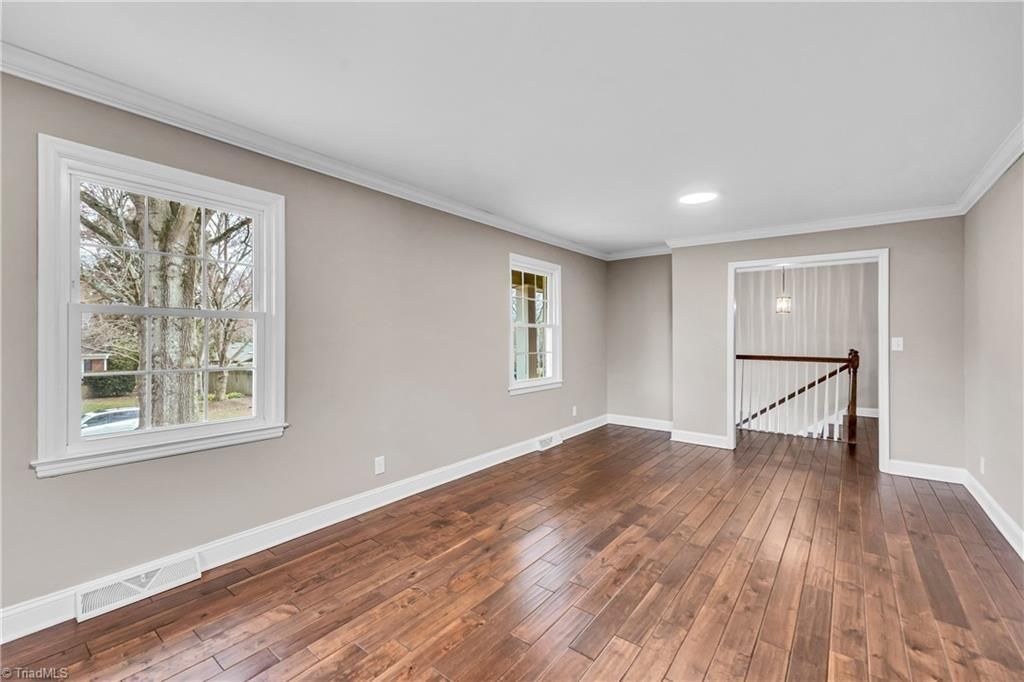 Empty living room with hardwood floors, gray walls, white trim, and two windows overlooking trees