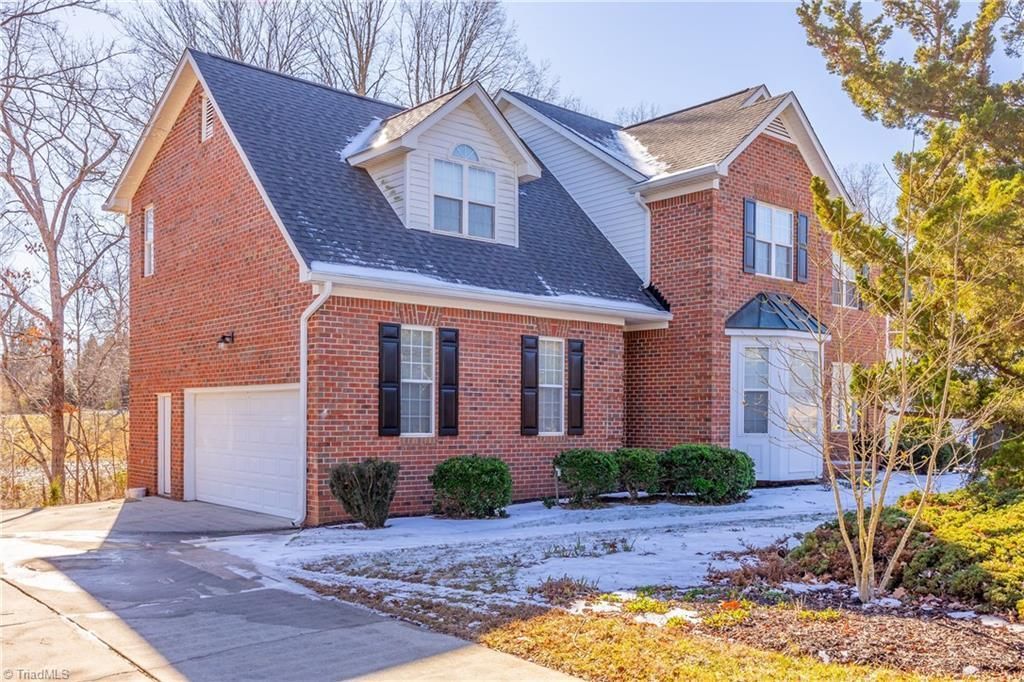 Brick house with a white garage and snow-covered yard on a sunny winter day