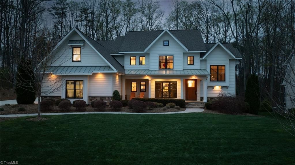Large white suburban house at dusk with lit windows and a dark green lawn.
