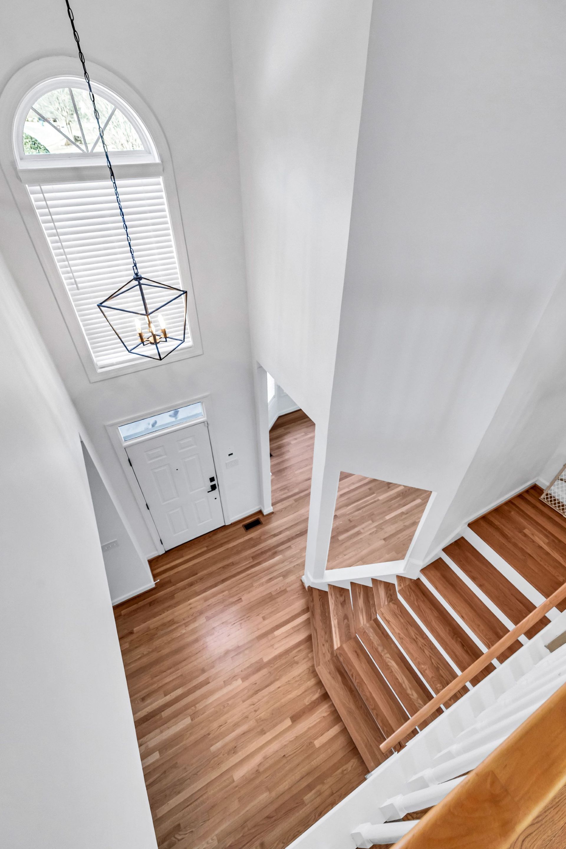 Bright white stairwell with wooden steps, tall arched window, and front entry door below.
