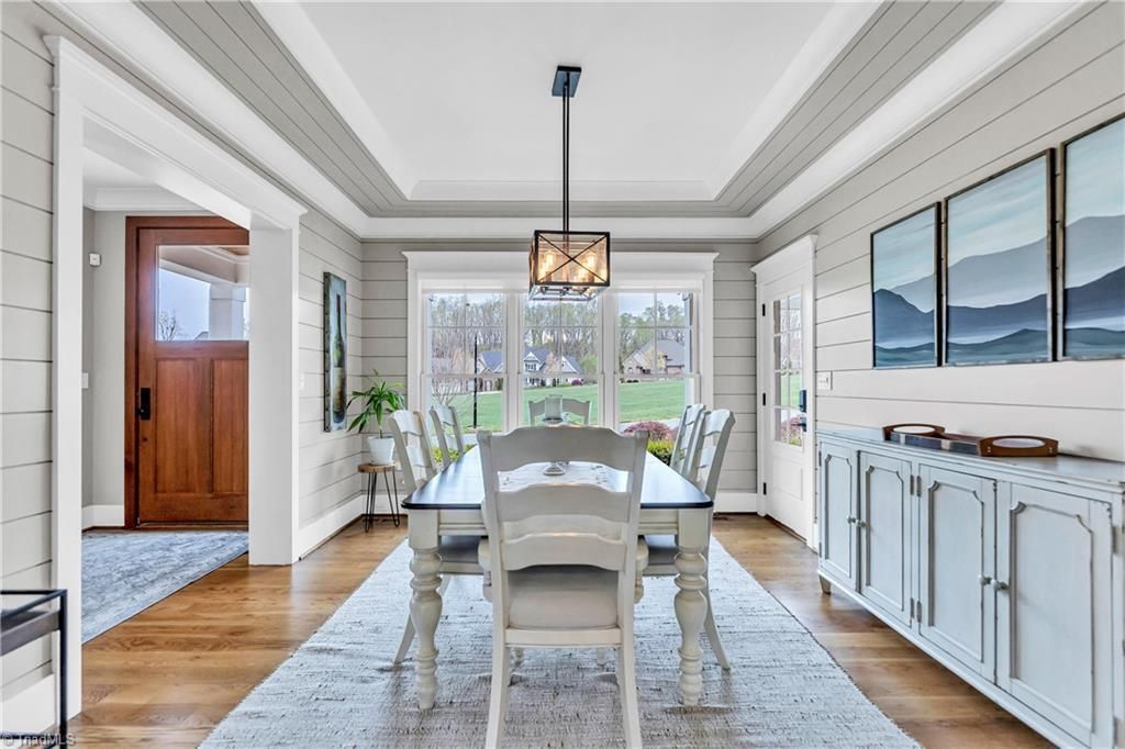 Bright dining room with white table, chairs, sideboard, and large windows overlooking greenery.