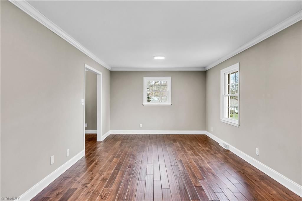 Empty living room with hardwood floors, beige walls, white trim, and two windows.