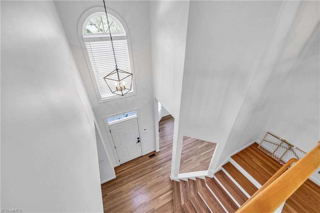 Bright white staircase foyer with wood steps and a tall arched window above the front door
