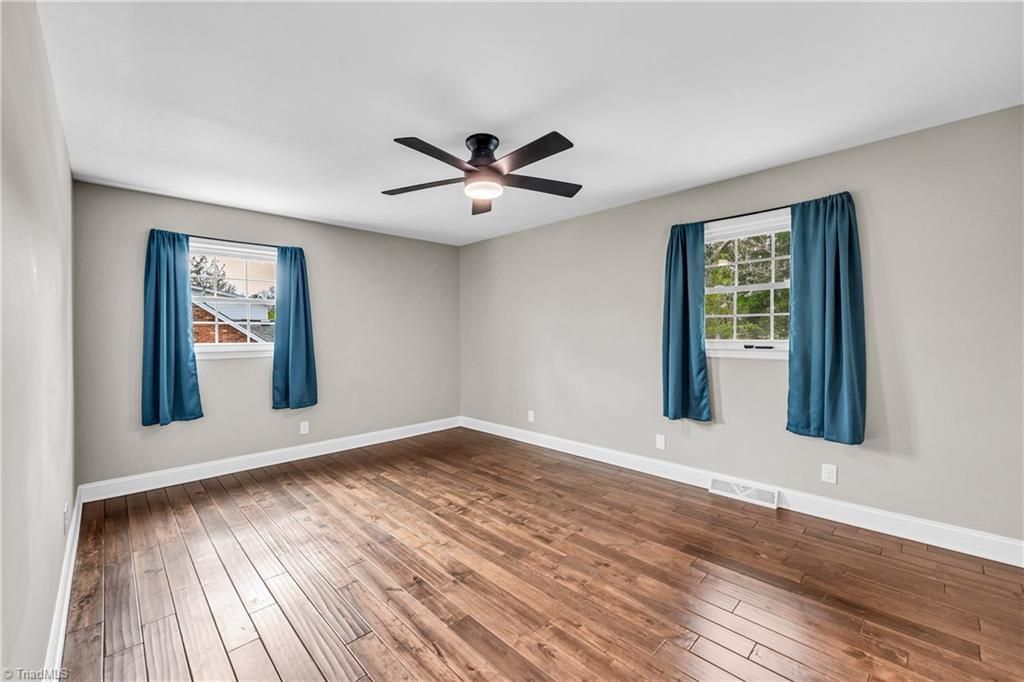 Empty room with hardwood floors, white walls, blue curtains, and a ceiling fan
