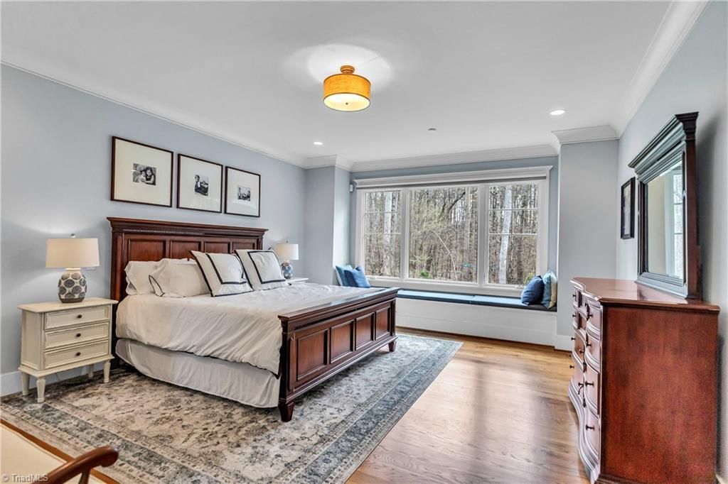 Bright bedroom with a wooden bed, patterned rug, dresser, and large bay window