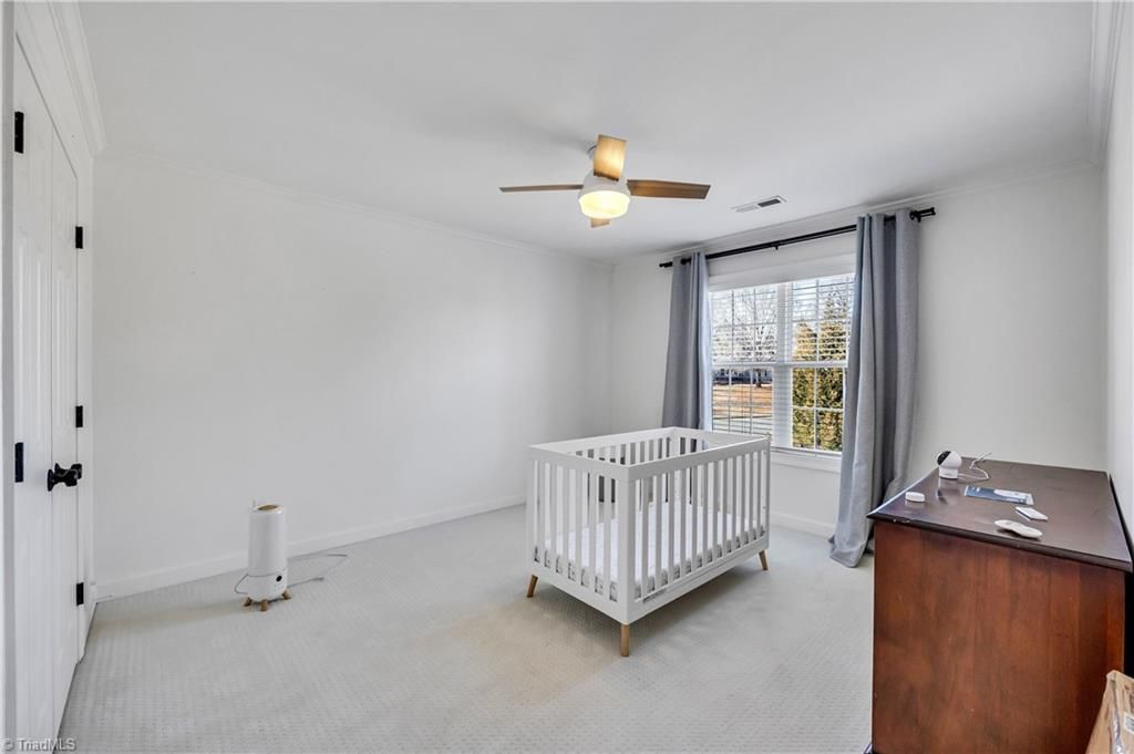 Bright nursery with white crib, ceiling fan, dresser, and large window with gray curtains