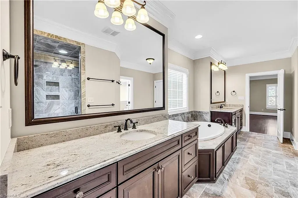 A bathroom with two sinks , a tub , and a large mirror.