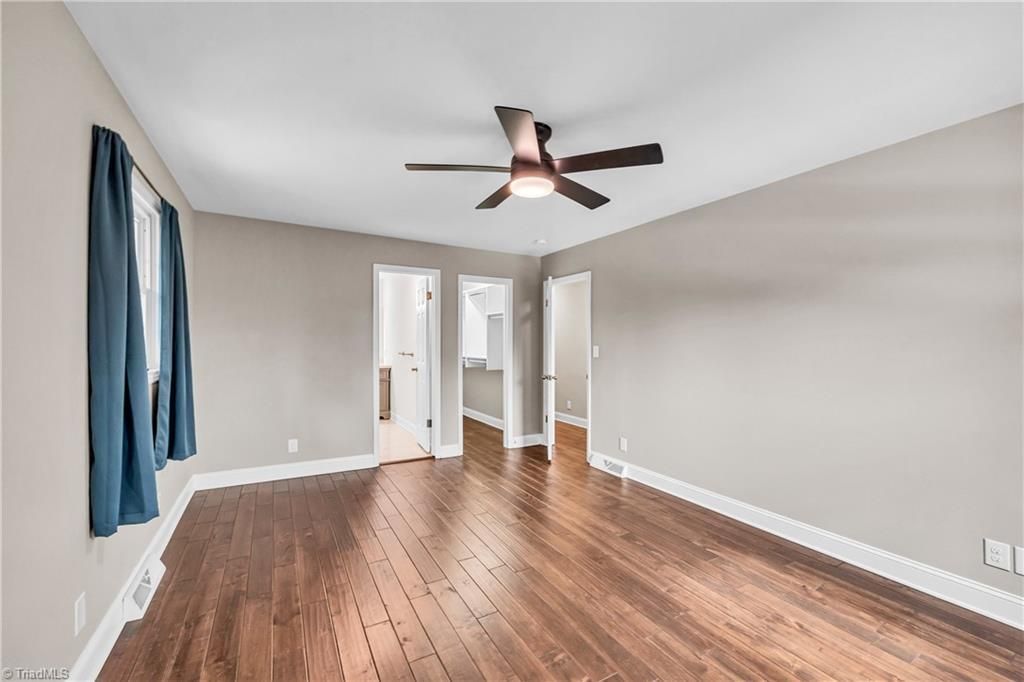 Empty bedroom with hardwood floors, beige walls, blue curtains, and a ceiling fan