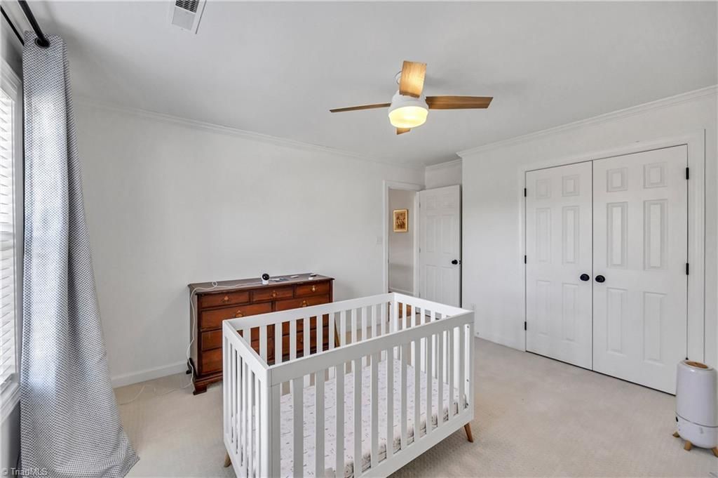 Bright nursery with white crib, dresser, ceiling fan, and double closet doors.