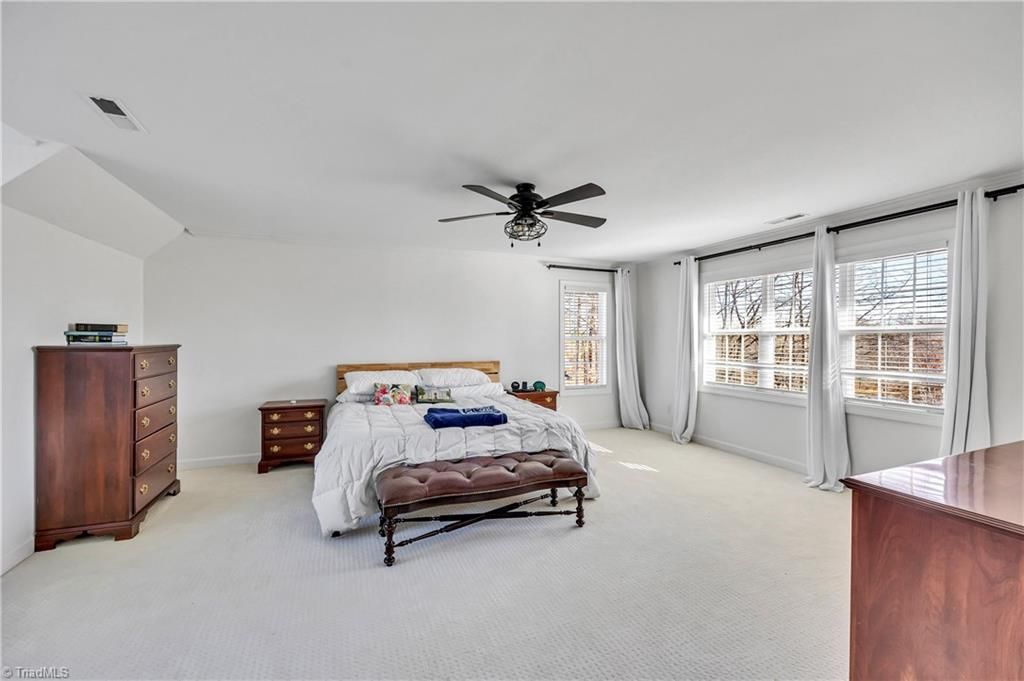 Bright bedroom with a bed, dresser, white carpet, ceiling fan, and large windows with curtains
