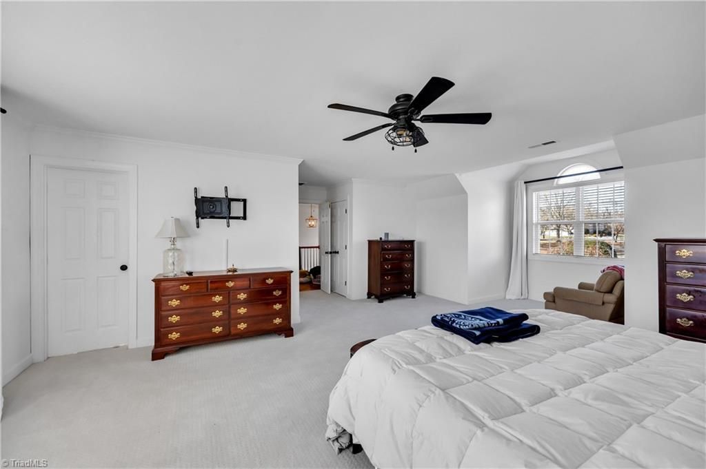 Bright bedroom with white walls, large bed, dresser, ceiling fan, and window seating area