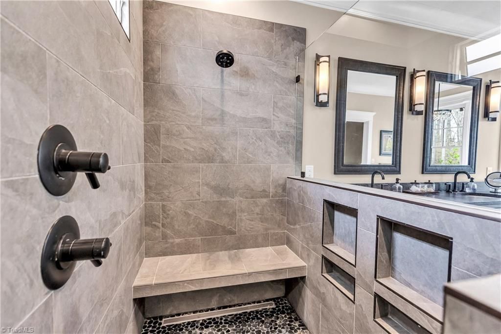 Modern bathroom with walk-in shower, gray tile, black fixtures, double vanity, and mirrors