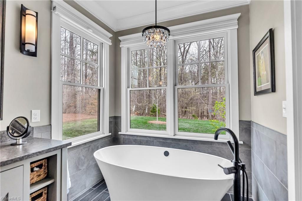 Bright bathroom with a freestanding tub, large windows, gray wainscoting, and a modern black faucet.