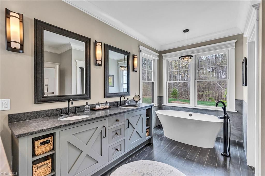 Modern bathroom with double vanity, large mirrors, and a freestanding tub by a window.