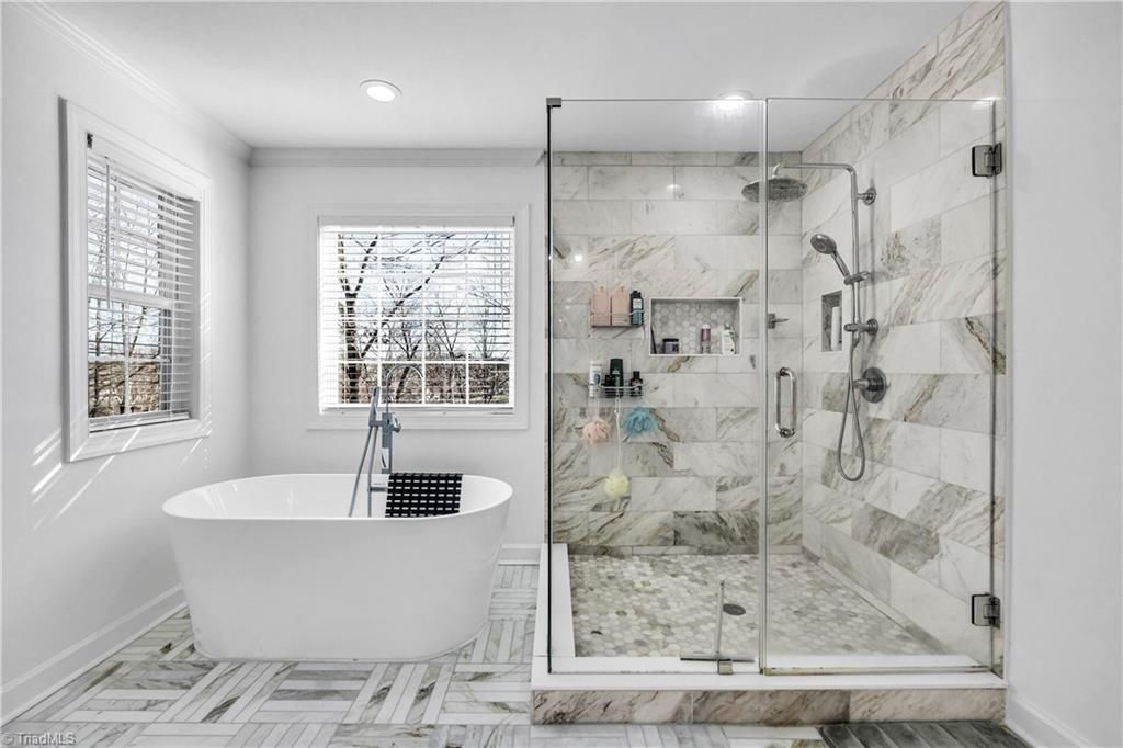 Bright modern bathroom with a freestanding tub, glass shower, and white marble-style tile walls and floor