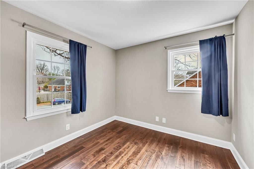 Empty room with gray walls, hardwood floor, and two windows with blue curtains
