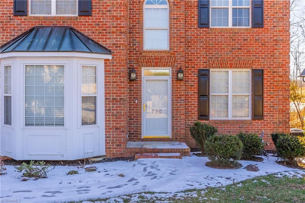 Brick townhouse entrance with snow-covered walkway, white front door, and windows on either side.