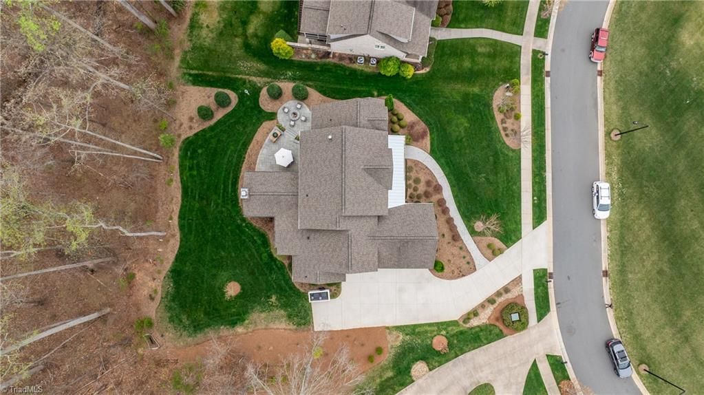 Aerial view of a suburban house with a curved driveway, lawn, and a road beside it