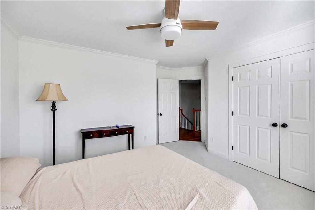 Bright bedroom with a bed, floor lamp, ceiling fan, open door, and white closet doors