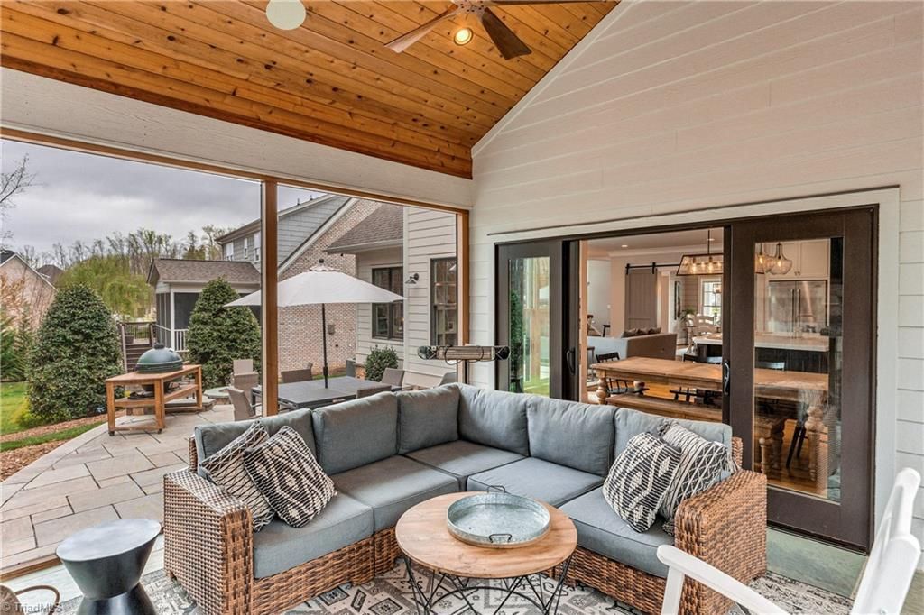 Covered patio with gray sectional sofa, wicker chairs, and mountain view through glass doors