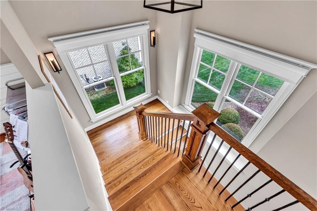 Bright staircase landing with hardwood floors, white walls, black railings, and large windows overlooking greenery
