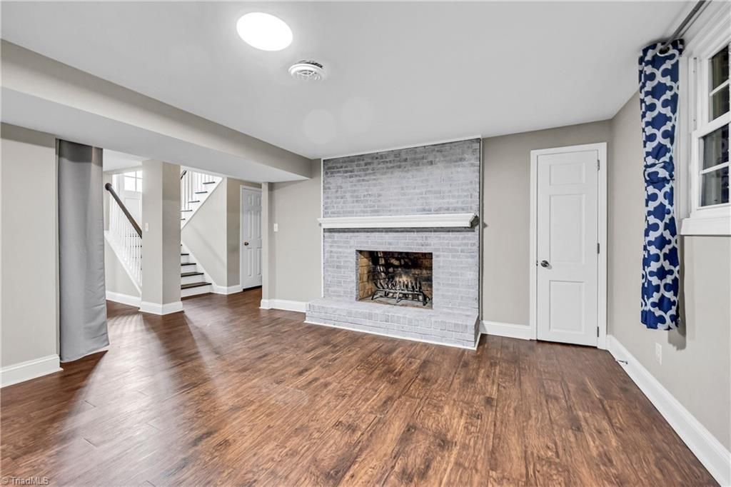 Empty living room with wood floors, gray walls, white fireplace, and blue curtains.