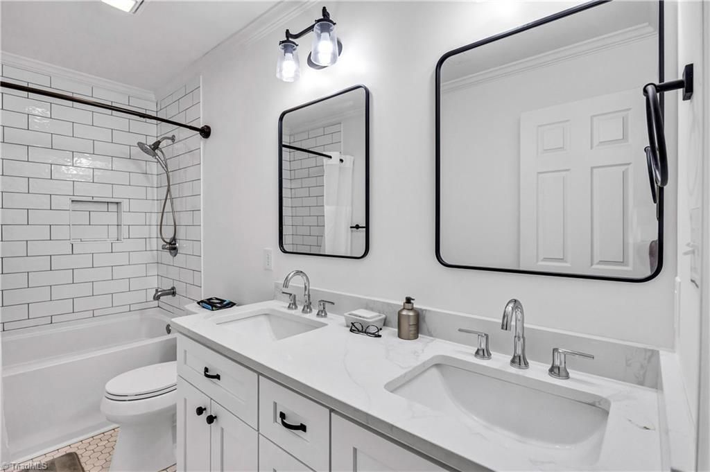 Modern white bathroom with double vanity, bathtub, and black-framed mirrors