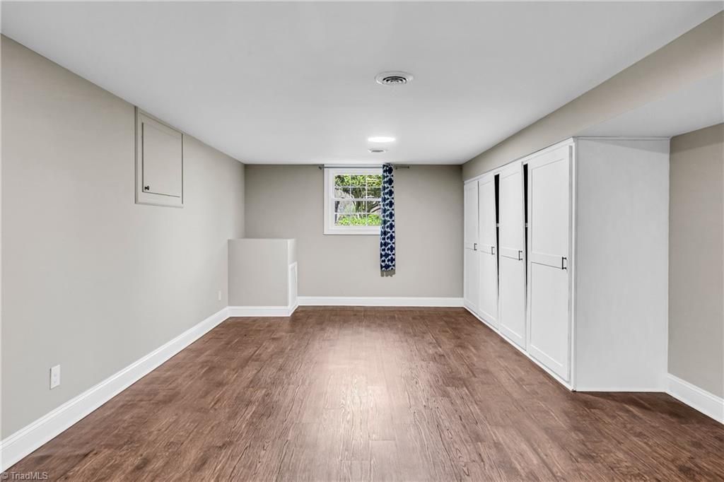 Empty finished basement room with gray walls, brown floor, white closet doors, and a small window.