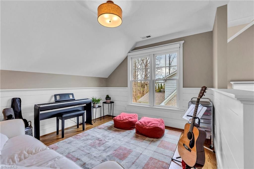 Cozy attic music room with piano, guitar, red poufs, and a window seat by a large window.