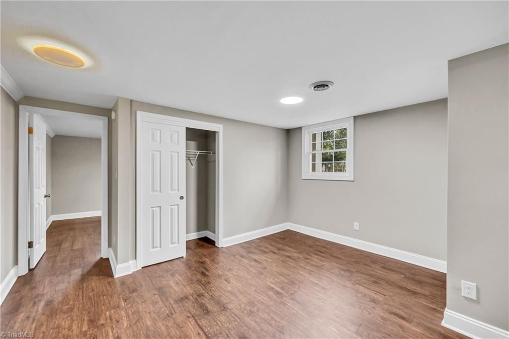 Empty beige bedroom with hardwood floors, white doors, and a small window.