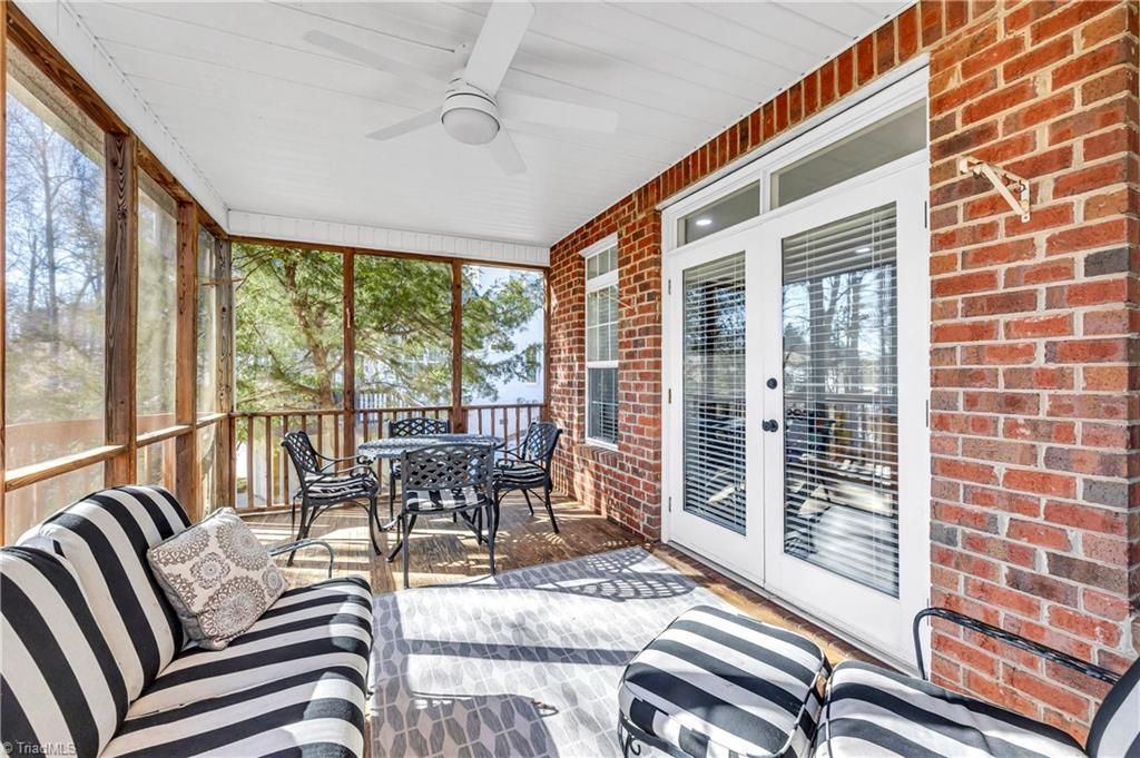 Screened porch with striped chairs, black table set, brick walls, and French doors overlooking trees