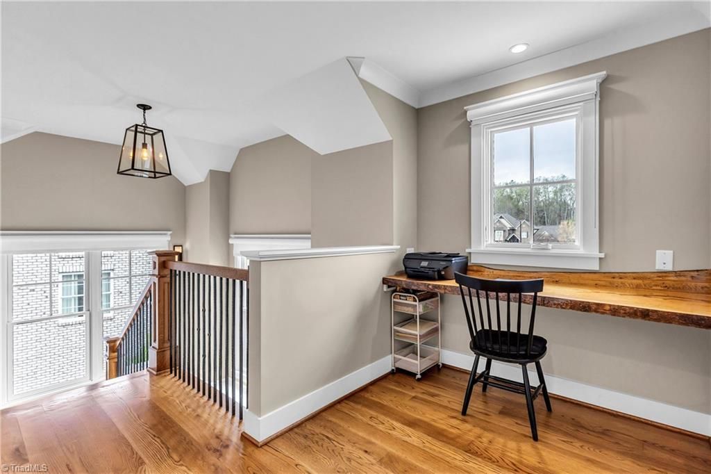 Stair landing with wood floor, built-in desk under a window, and black chair in a bright beige interior