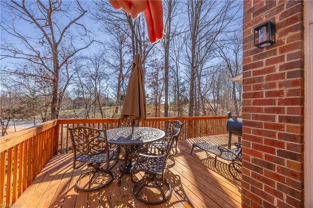 Wooden deck with patio table, chairs, umbrella, and brick house wall overlooking bare trees