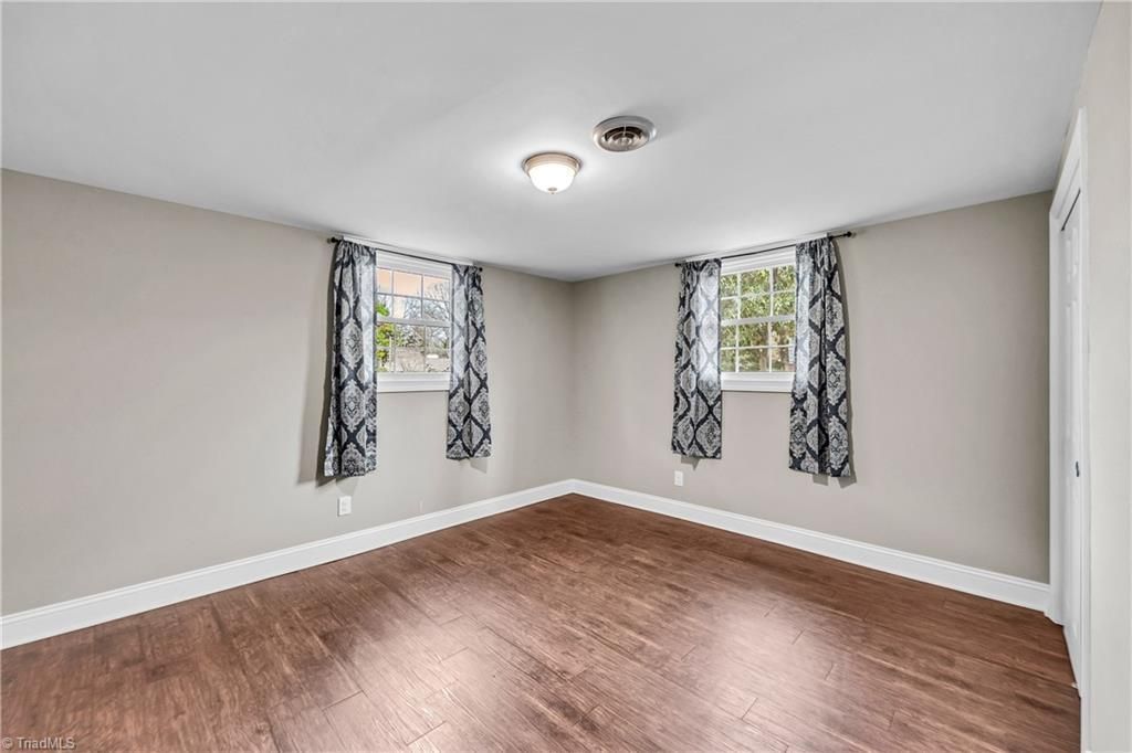 Empty room with hardwood floors, beige walls, and two windows with patterned curtains.