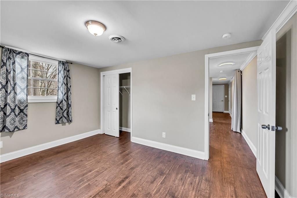 Empty bedroom with hardwood floors, gray walls, white trim, two windows, and an open doorway to a hallway