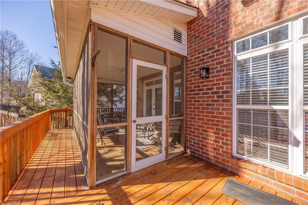 Sunlit wooden deck beside a brick house with screened porch and white-framed windows