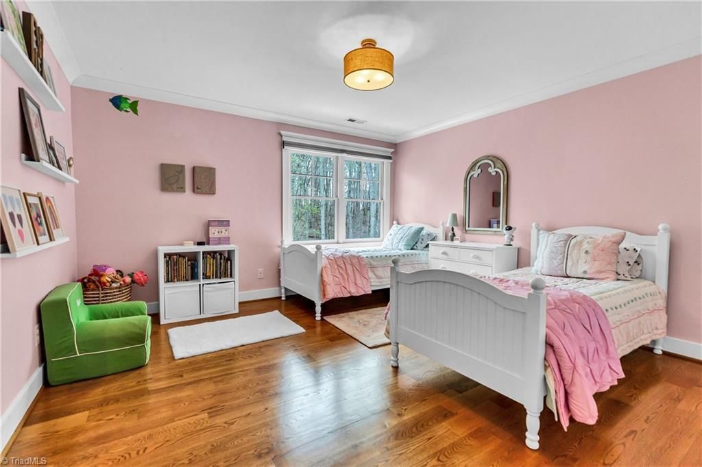 Pink bedroom with white bed, hardwood floors, green chair, and window seating area