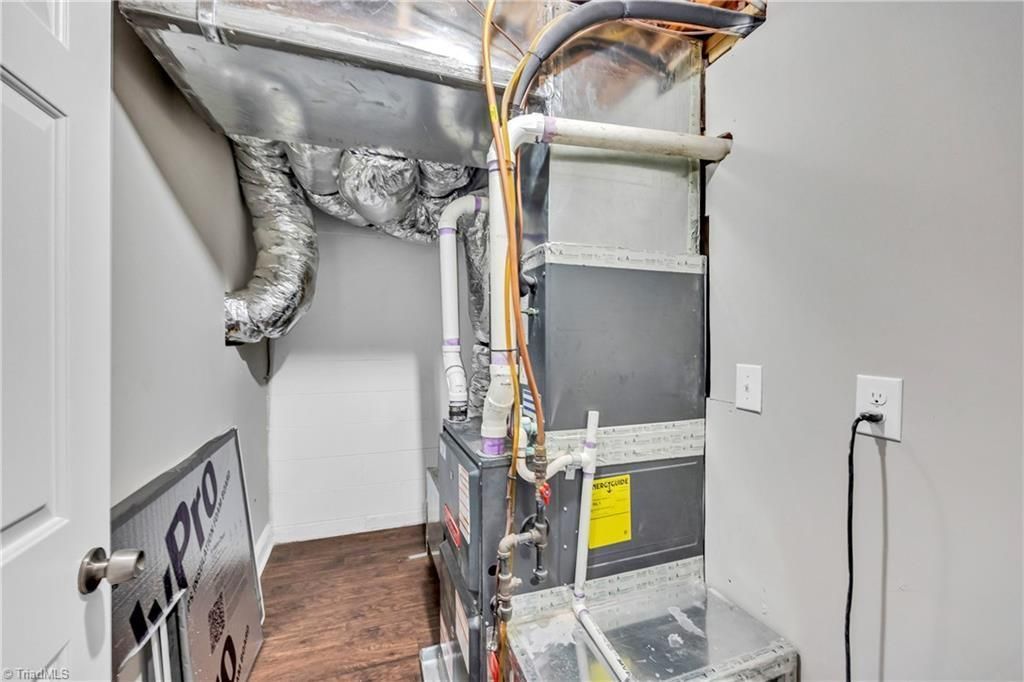 Utility room with HVAC equipment, exposed ducts, and a wall-mounted electrical outlet.