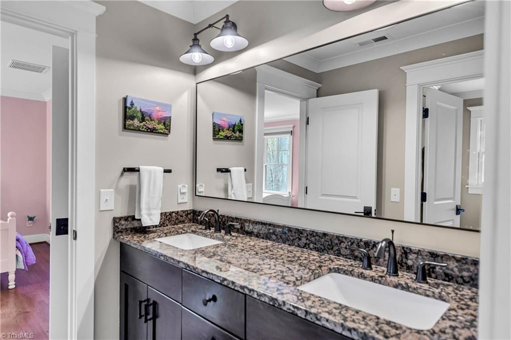 Modern bathroom with granite double vanity, large mirrors, and overhead lights