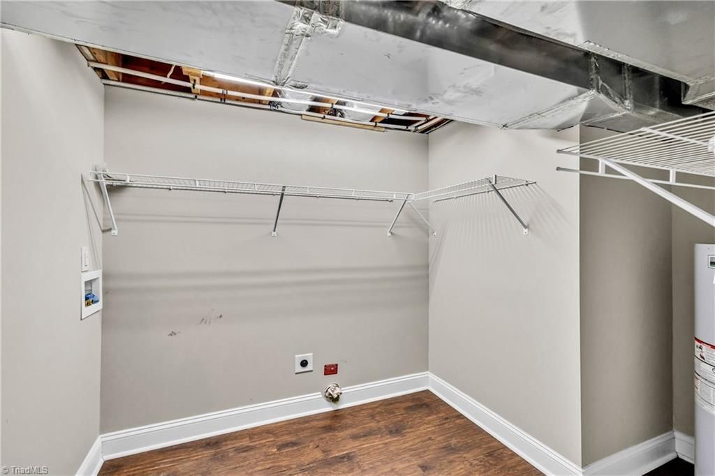 Empty white walk-in closet with wire shelving and a brown floor, shown with exposed ceiling damage