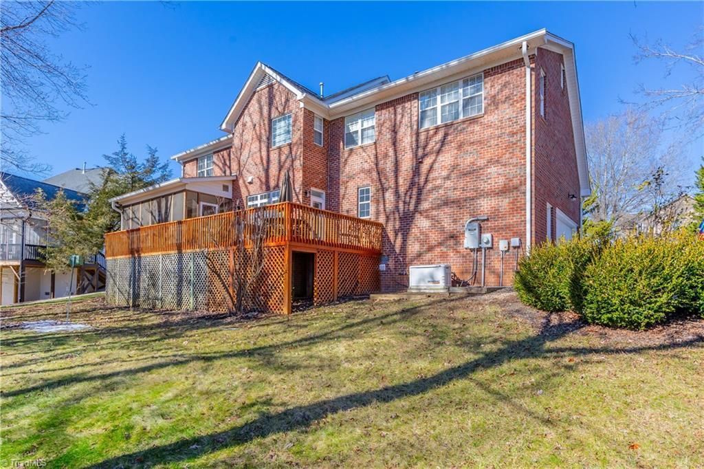 Brick apartment building with wooden balcony and grassy front lawn under a clear blue sky