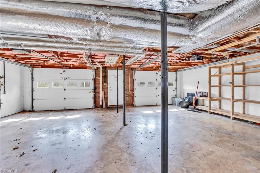 Empty unfinished basement with exposed ceiling pipes and framing, concrete floor, and a central support post