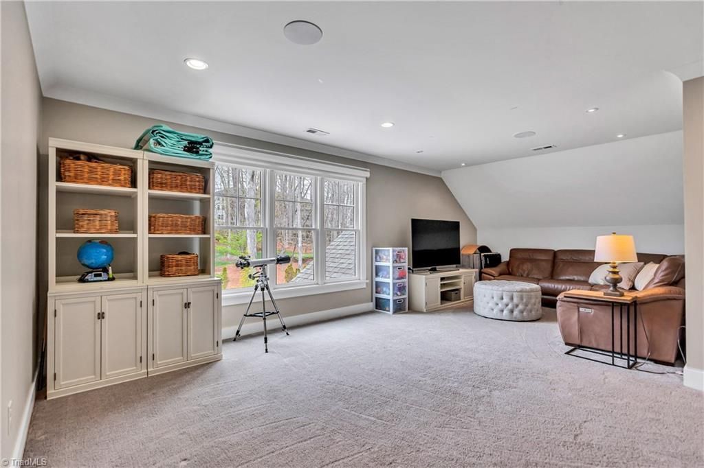 Bright living room with shelves, a TV, armchairs, and large window with a tripod near the center