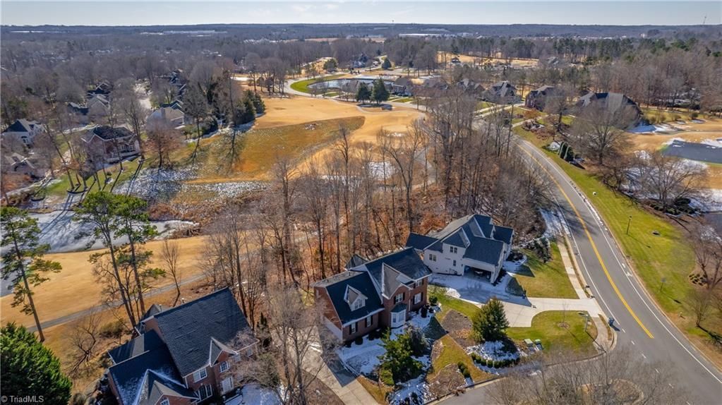 Aerial view of suburban homes beside a road and winter-brown parkland with trees and fields.