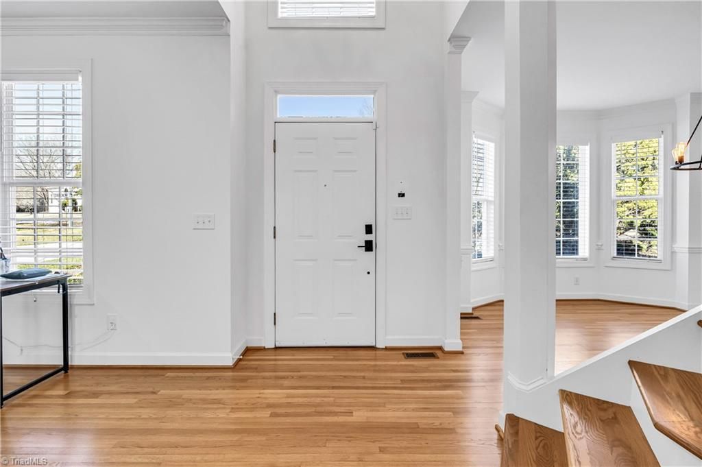 Bright entryway with white walls, hardwood floors, front door, and large windows letting in daylight