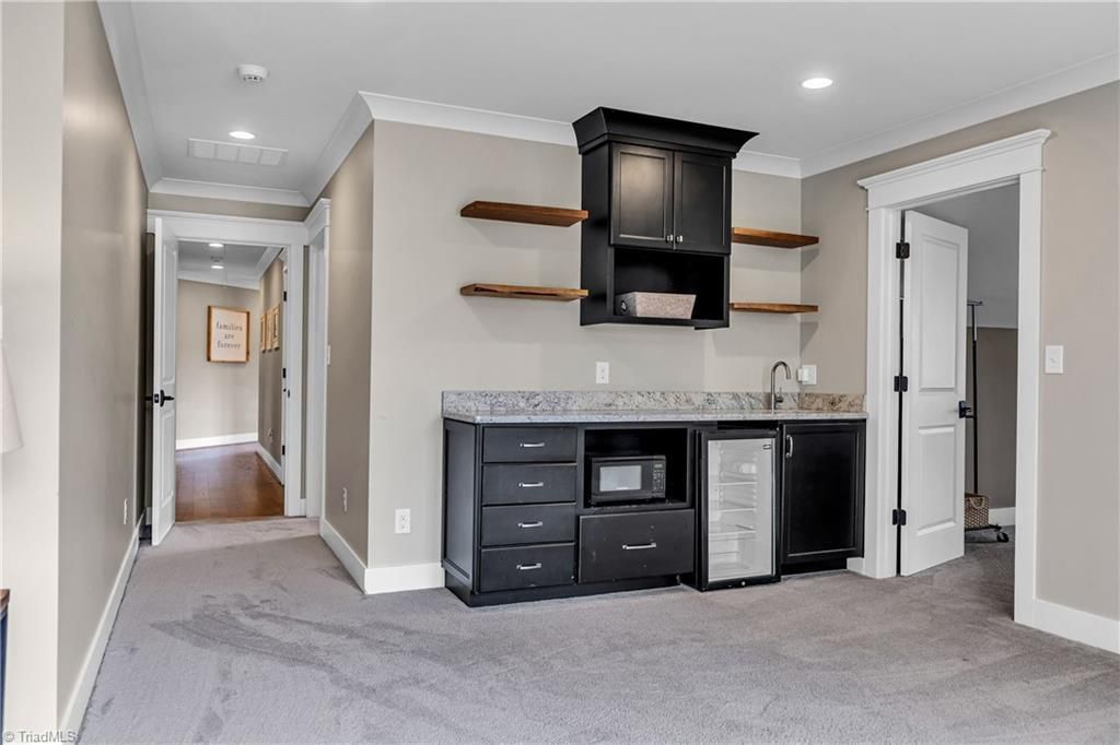 Empty carpeted room with gray walls, black built-in cabinetry, shelves, and a doorway to a hall
