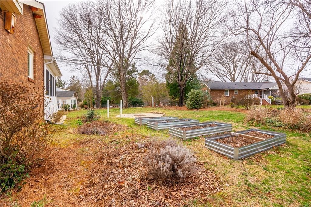 Leaf-covered yard with raised garden beds beside a brick house in autumn.